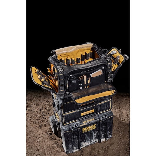 DEWALT tool bag with compartments, open on top of black storage boxes, placed on dirt.