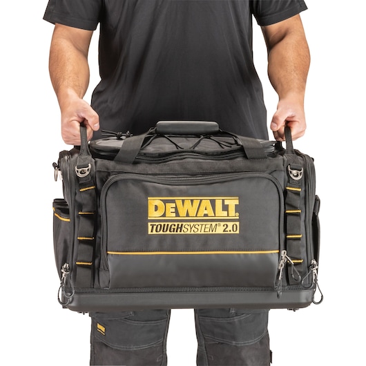 A person holding a DEWALT ToughSystem 2.0 tool bag by its handles. The black and yellow DEWALT branded bag is shown in front view.