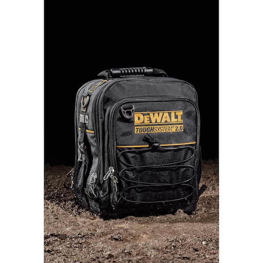 DEWALT ToughSystem 2.0 black tool backpack with yellow accents sits on dirt.