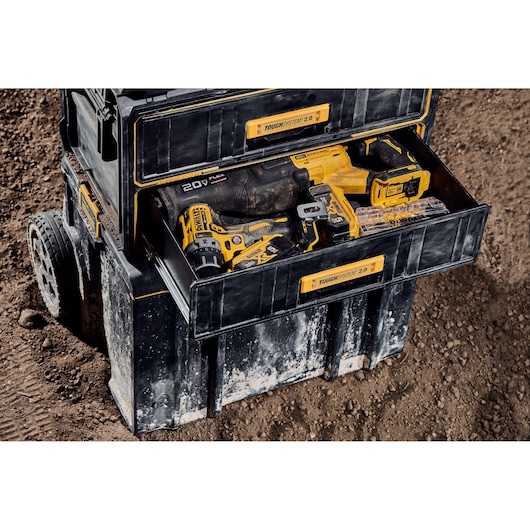 A black DEWALT ToughSystem 2.0 tool storage box on wheels, opened to show yellow DEWALT power tools and accessories inside, placed on a dirt surface.