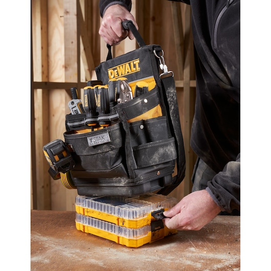 DEWALT tool bag with tools set on yellow stackable organizers on a workbench, handled by a person in workwear.
