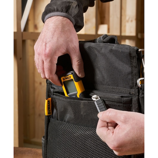 Hand places DEWALT device and tool bit into black zippered bag pocket in a workshop setting.