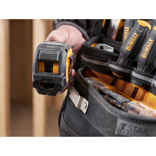 Close-up of a DEWALT tool belt with hand holding tape measure and screwdrivers in pockets.