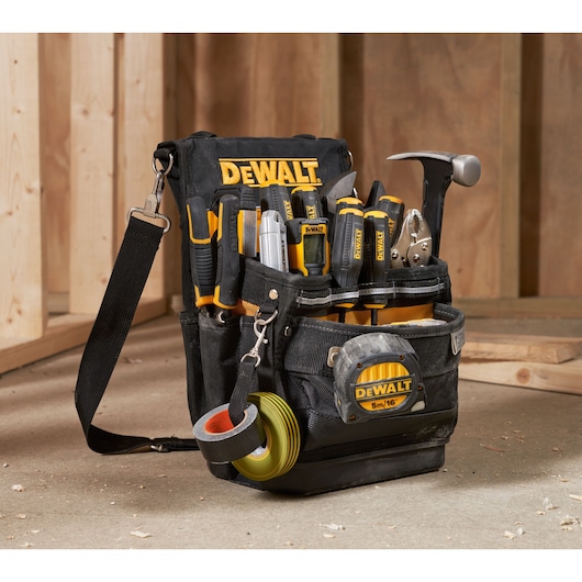 DEWALT tool bag with hand tools, tape measure, and rolls of tape, placed in a workshop setting.