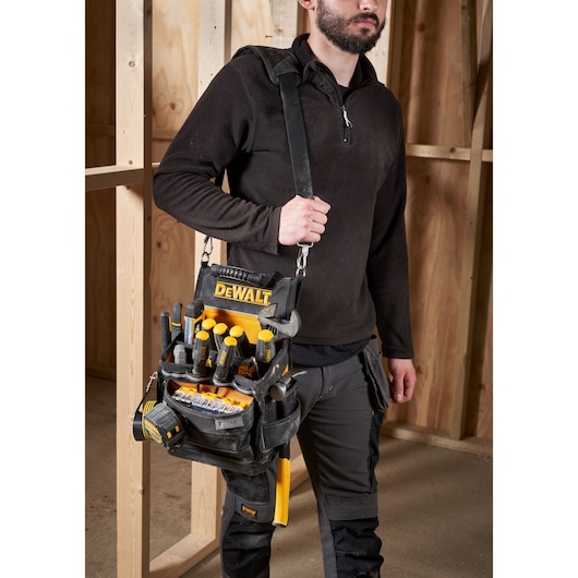 Person carrying a DEWALT tool bag filled with hand tools in a workshop.