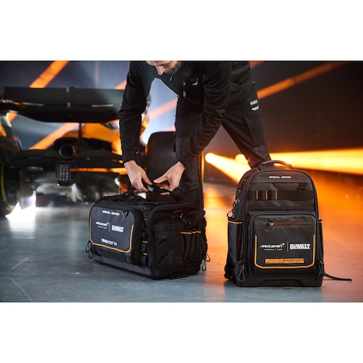 Person with DEWALT tool bag and backpack, labeled as Special Edition, near a race car in a garage with orange lights.
