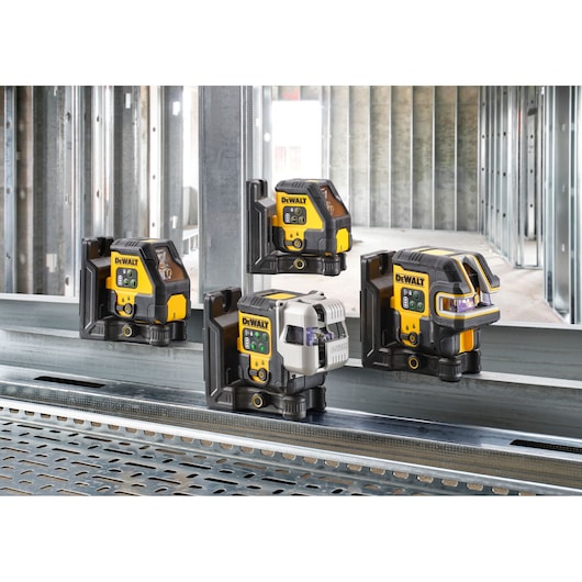 Four DEWALT laser levels are displayed side by side on a metal beam at a construction site, with unfinished metal stud framing in the background.