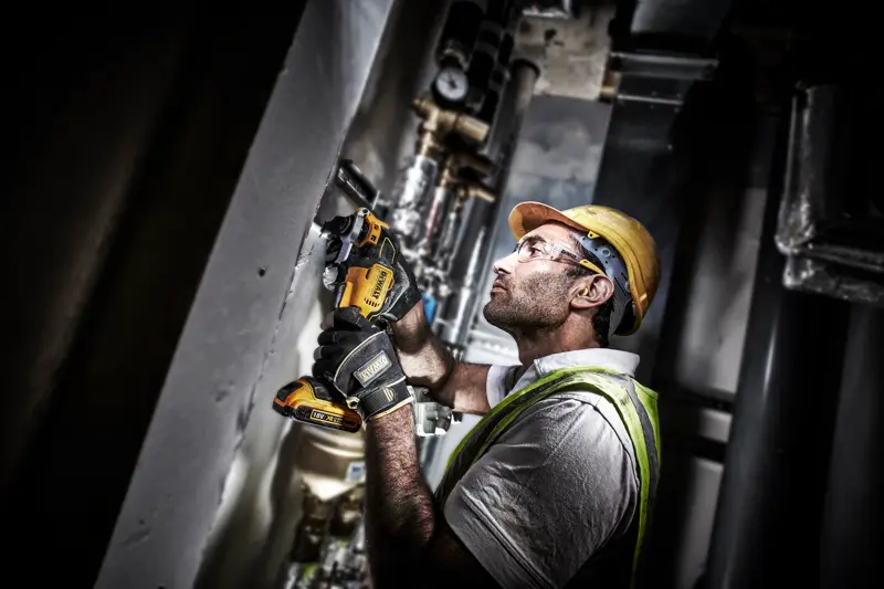 Ouvrier utilise un outil DEWALT DCS355D2 sur un mur, équipé de protections et de gants de sécurité.
