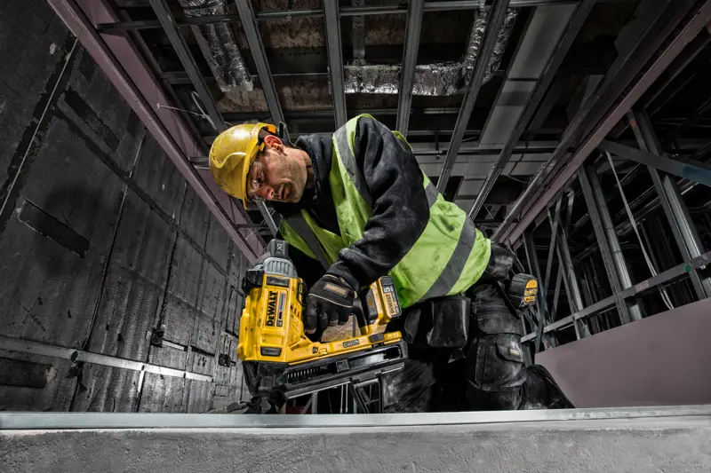 Ouvrier avec cloueuse DEWALT DCN890P2 sur chantier, portant casque et gilet de sécurité.