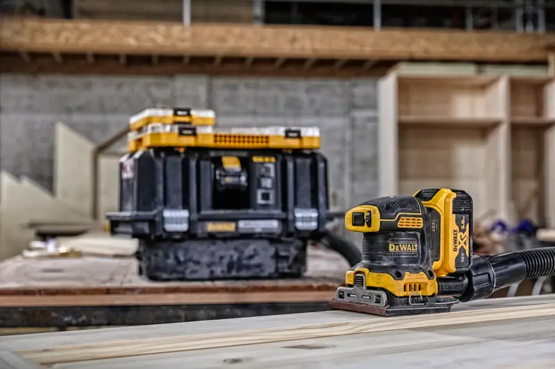 Ponceuse sans fil DEWALT sur bois, boîte de rangement en arrière-plan dans un atelier.
