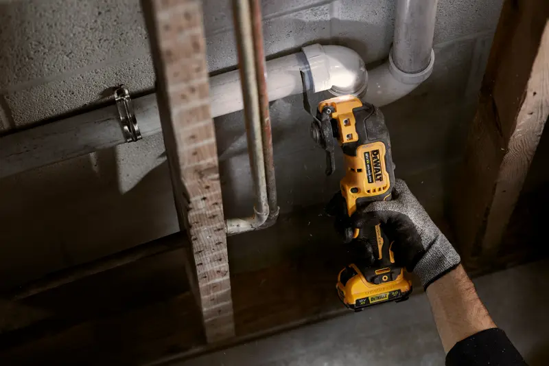 Une personne coupe un tuyau avec un outil oscillant DEWALT sans fil contre un mur en béton.