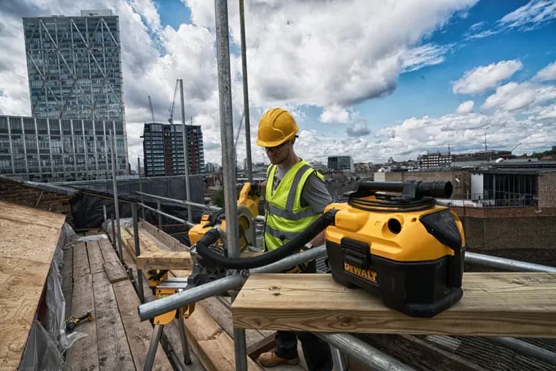 Aspirateur DEWALT DCV584 sur un chantier en hauteur avec un ouvrier équipé et des bâtiments urbains en arrière-plan.