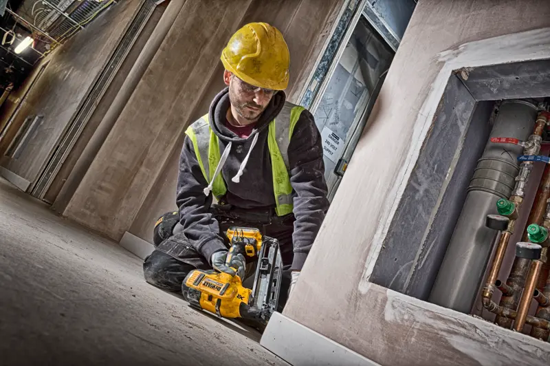 Ouvrier utilise une cloueuse DEWALT DCN660N, casque jaune et gilet de sécurité sur chantier.