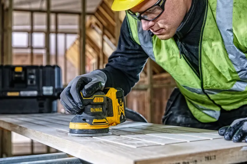 DEWALT DCW210, DCW210D1 ponceuse utilisée sur bois au chantier. Personne avec gants et gilet de sécurité.