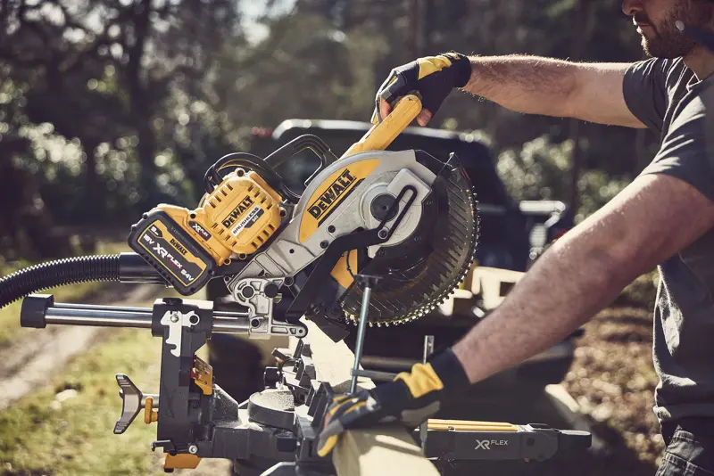 Personne coupant du bois dehors avec une scie à onglets DEWALT sans fil, outil jaune-noir, batterie XR FLEXVOLT.