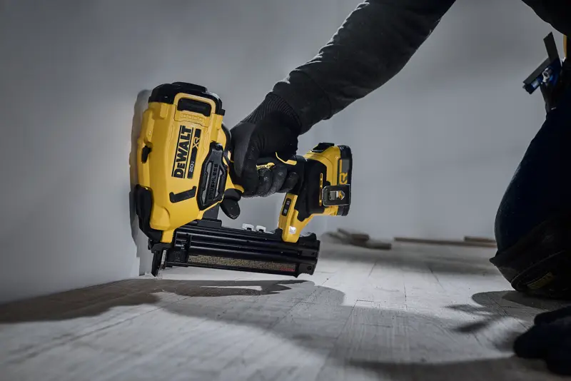Une personne utilise un cloueur sans fil jaune et noir DEWALT DCN210 pour fixer une moulure en bois le long du bas d’un mur.