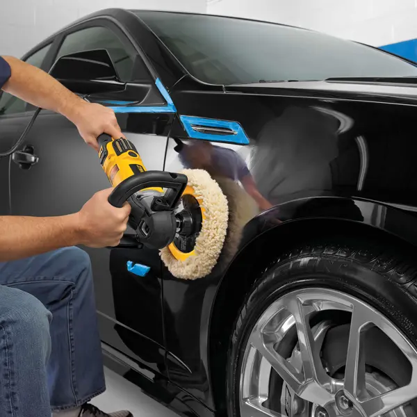 Une personne polit l’aile d’une voiture noire avec une polisseuse DEWALT.