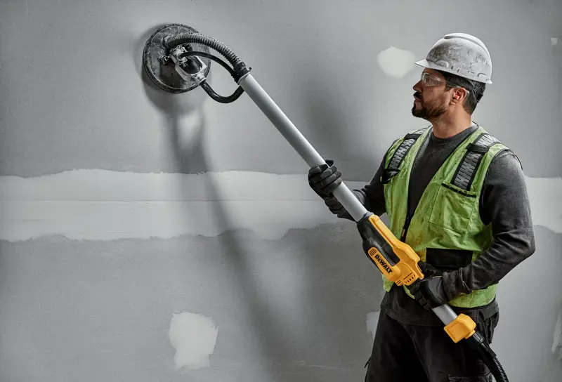 Ouvrier avec ponceuse murale DEWALT DWE7800, DWE7800-QS sur plaque de plâtre. Produit de photographie.