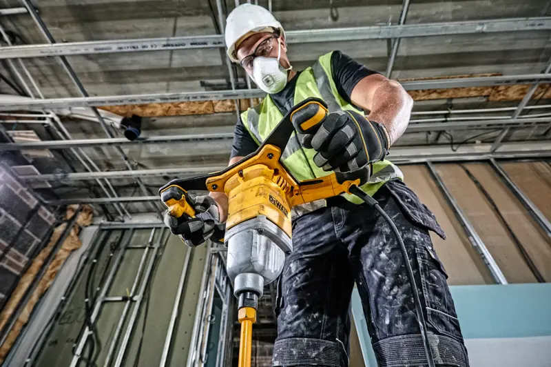 Personne utilise une perceuse-mélangeuse DEWALT DWD241 sur chantier, équipée de gilet et gants de sécurité.