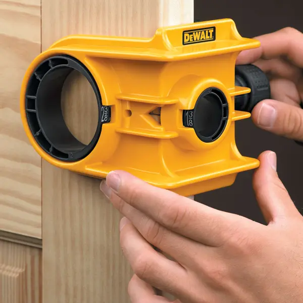 Une personne utilise un kit d'installation de serrure de porte DEWALT jaune pour aligner et marquer un trou sur un cadre de porte en bois.