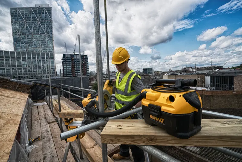 Aspirateur DEWALT DCV584 sur un chantier en hauteur avec un ouvrier équipé et des bâtiments urbains en arrière-plan.
