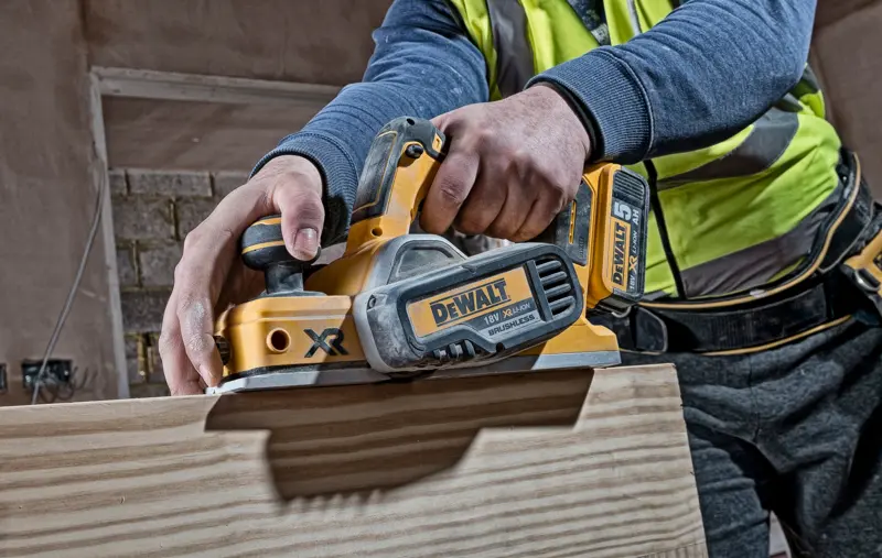 Personne utilisant un rabot sans fil DEWALT DCP580N sur une surface en bois sur un chantier.