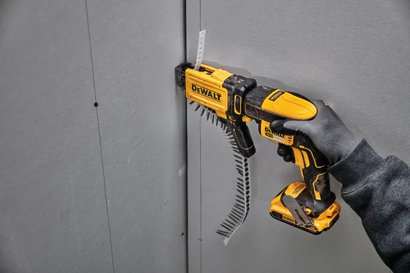 Visseuse DEWALT DCF6202 vissée dans du placo, tenue par une main gantée sur un panneau mural.