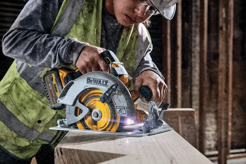 Scie circulaire sans fil DEWALT coupe du bois, utilisée par un ouvrier portant un gilet sur un chantier.